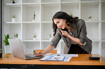 Professional and busy Asian businesswoman looking at laptop screen while talking on the phone