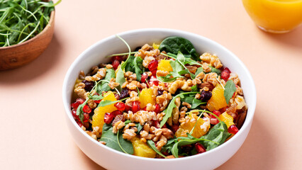 Healthy salad with spelt, oranges, pomegranate seeds. greens and nuts on light background, minimal style