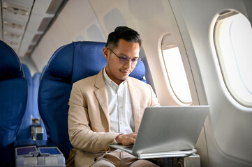 A professional and focused businessman using a laptop during the flight. - Powered by Adobe