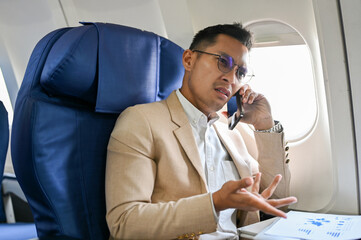 Stressed Asian businessman is having a serious conversation on the phone during his flight