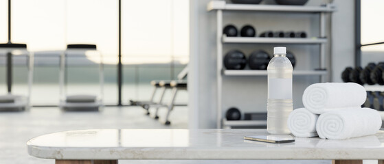Copy space on white tabletop with a bottle of water, towels over modern fitness center