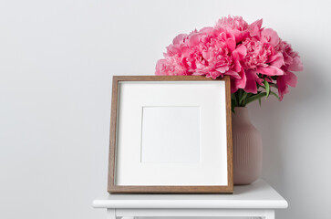 Square wooden frame mockup with pink peony flowers in white room interior