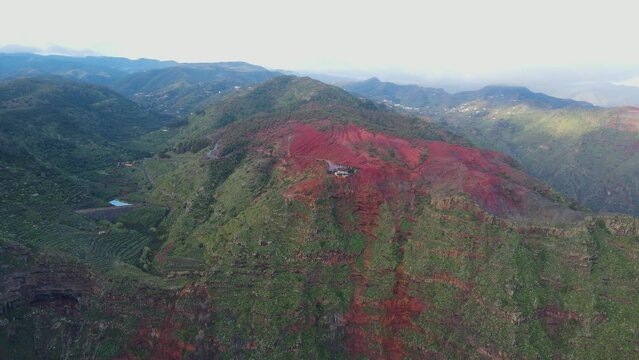 Aerial view of stunning viewpoint Mirador de Abrante with glass observation balcony above Agulo village in La Gomera island at sunrise. Restaurant on red clay.
