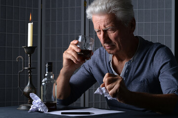 Caucasian old man with bottle of alcohol sitting in room and writing
