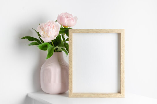 Picture frame mockup with pink peony flowers in white room, blank mockup for artwork, photo or paintings