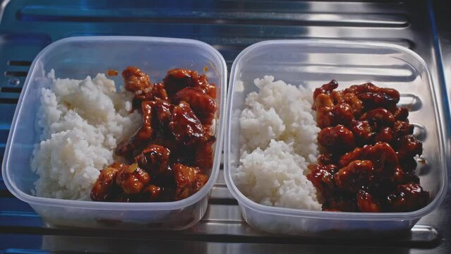 Tuppers of chicken and rice ready to eat in a kitchen, close up view with zoom out.