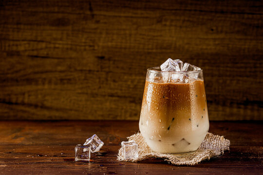 Glass of iced coffee with milk on dark wooden background, side view, copy space. 