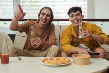 Joyful young men drinking beer when watching soccer game at home