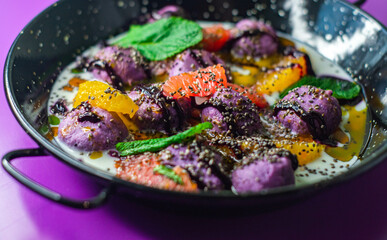 Breakfast in black plate on purple background with lazy cheesecakes currant, strawberry, blueberry, chia, mint and coconut sauce.