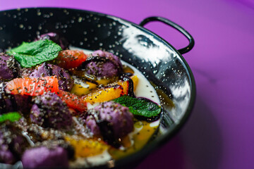 Breakfast in black plate on purple background with lazy cheesecakes currant, strawberry, blueberry, chia, mint and coconut sauce.