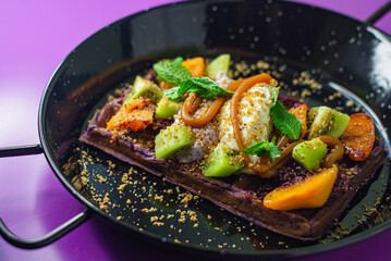 Belgium chocolate waffle with fruit and ice cream, caramel. Sweet peach and kiwi decorated mint.