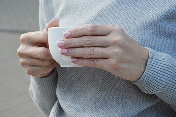 A girl in a gray sweater holds a cup of tea or coffee in her hands.