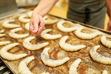 Hand of baker sprinkles croissants with poppy seeds