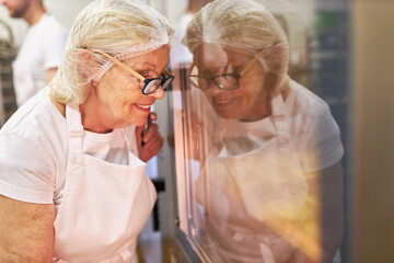 Elderly baker at the oven controls baking