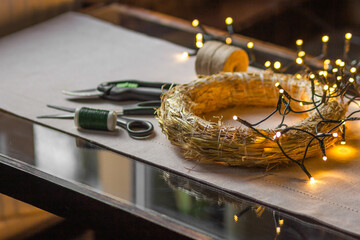 Florist's workplace with professional tools: pruner, sciccors, spool of thread and wire, eco straw base with garland.
