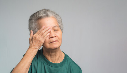 Portrait of a senior woman with eye pain while standing on a gray background