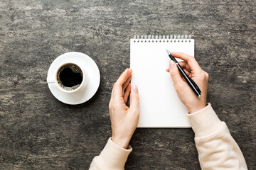 Woman hand with pencil writing on notebook and hold coffee cup. Woman working on office table with...