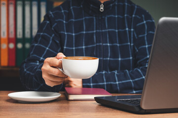 Businessman in a sweater hand holding a cup of coffee while sitting and working at the table