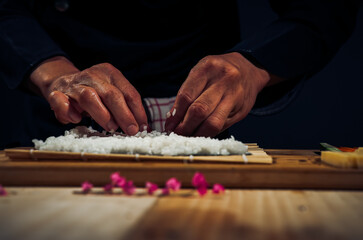 Japanese chef making California Maki Sushi with Masago - Roll made of Crab Meat, Avocado, Cucumber inside. Masago (smelt roe) outside with tuna, salmon, shrimp,traditional Japanese food ,Dark Tone