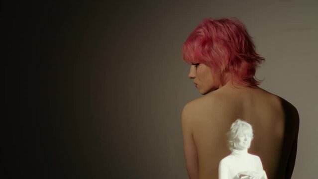 Conceptual studio portrait of sad young gen Z woman with pink hair suffering depression or bipolar disorder with her happy image projected on her back