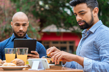 african american gay couple having breakfast and looking at mobile outside in the garden
