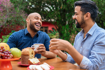 african american gay couple laughing and having breakfast in table outside