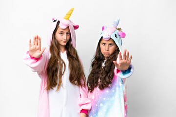 Friends girls with unicorn pajamas over isolated white background making stop gesture denying a...