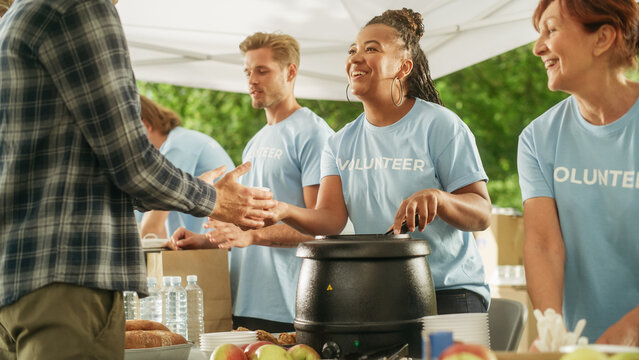 Positive Group Of Young Adult Volunteers Serving Free Food For Poor People In Need. Charity Workers Help Members Of The Community. Humanitarian Aid To Refugees And Immigrants.