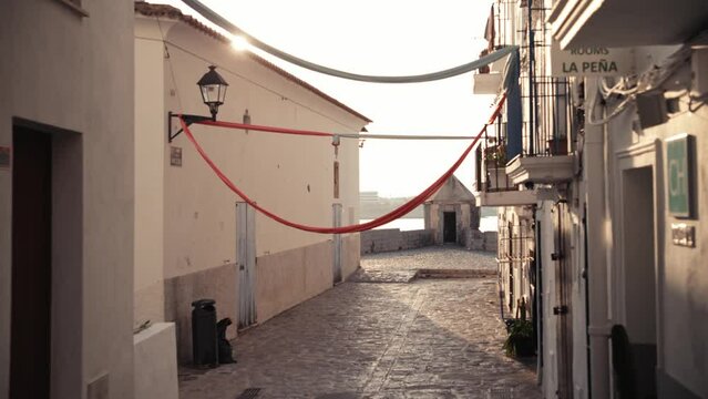 A beautifully decorated street in Ibiza ends by the sea with the sun shining in the background