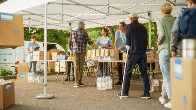 Establishing Shot of a Group of Volunteers Handing Out Food Rations for Poor People in Need. Charity Workers and Members of Community Work Together. Concept of Giving, Humanitarian Aid and Society.