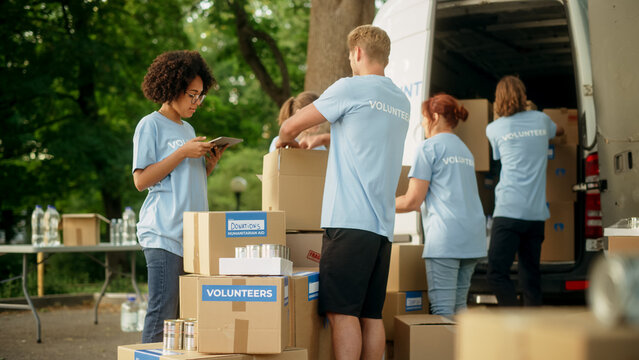 Group of Hardworking Volunteers Preparing Donated Free Food Rations, Loading Packages in a Cargo Van on a Sunny Day. Charity Workers Work in Local Humanitarian Aid Organization.