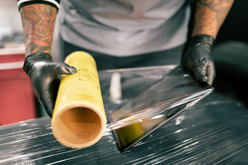 A tattoo artist is covering his work tablet with plastic film