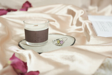 coconut wax candle in a glass with wooden wick on a plate on silk bedding. romantic valentine's morning with scented candle.