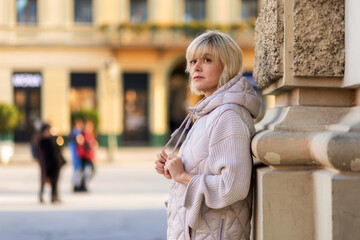 Fototapeta premium Portrait of adult alone Caucasian woman posing at column in city square. Copy space. Concept of psychology and loneliness