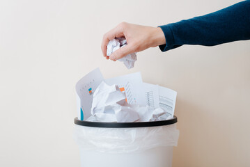 Close-up of an office worker's hand throwing crumpled paper documents into a trash can, indoors
