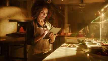 Tuinposter In Restaurant: Beautiful Female Chef Using Laptop Computer. Authentic Pizza Place Cooking Delicious Organic Eco Food. Bi-racial Female Entrepreneur Working on Online Order, Small Business Family Shop © Gorodenkoff