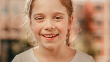 Fototapeta premium Close Up Portrait of an Adorable Little Girl with Brown Eyes and Hair Looking at Camera, Smiling Happily. Smart Talented Girl Laughing and Having Fun at Home. Soft Bokeh Background.