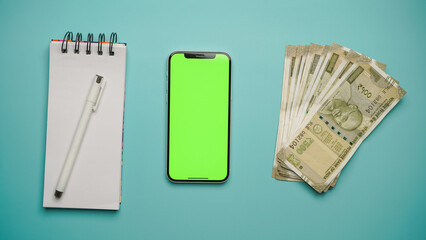 Top above flat lay view of a green screen mobile phone, Indian rupees currency over isolated blue colour background studio shot