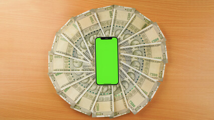 Top above flat lay view of a green screen mobile phone over Indian rupees, currency background isolated studio shot