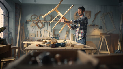 Young Happy Carpenter Assembling Parts of a Wooden Chair. Professional Furniture Designer Working in a Workshop in Loft Space with Tools on the Walls.