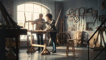 Obraz na płótnie Canvas Adult Carpenter and a Young Multiethnic Female Apprentice Working in Loft Studio on a New Chair Design. Small Business Owners Talking About Work in a Stylish Furniture Workshop.