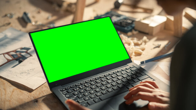 Over the Shoulder Shot of a Furniture Designer Working on Laptop Computer with Green Screen Mock Up Display. Creative Female Preparing a Design for Carpentry Project.