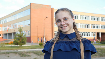 A teenage girl wearing glasses in front of a school.