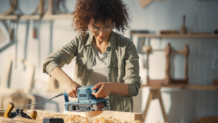 Portrait of a Talented Beautiful Artisan Carpenter Using Electric Sanding Machine to Polish a Wood Bar. Female Artist or Furniture Designer Working on a Project in a Loft Studio with Tools on Walls.