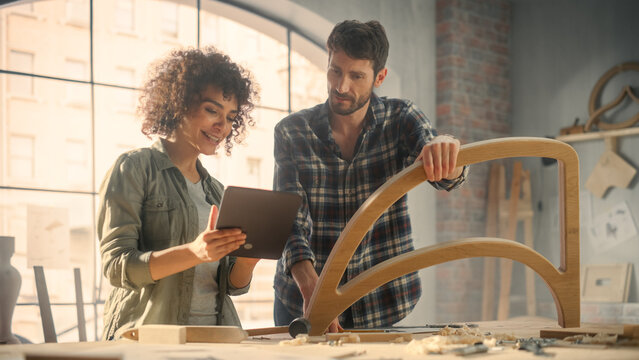 Excited Young Man and Woman Using Tablet Computer, Discussing a Successful Project in a Carpentry Studio. Furniture Designers Working in Loft Studio.