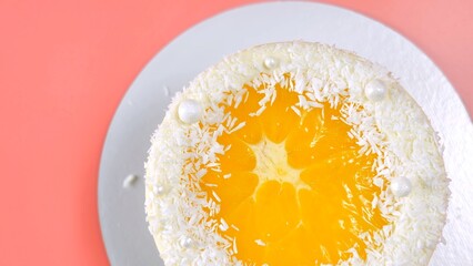 Cake with orange and coconut shavings spun on a pink background.
