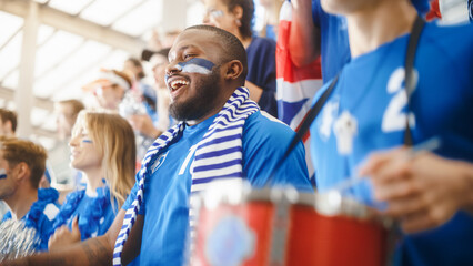 Obraz na płótnie Canvas Sport Stadium Big Event: Handsome Black Man Cheering. Crowd of Fans with Painted Faces Cheer, Shout for the Blue Soccer Team to Win. People Celebrate Scoring a Goal, Championship Victory