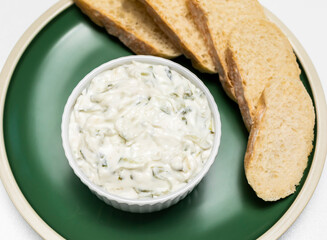 Traditional homemade greek yogurt sauce Tzatziki, tarator in white bowl, made of grated cucumbers, sour cream yogurt,olive oil,garlic,herbs on plate with sliced bread, white background.Horizontal