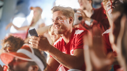 Sport Stadium Soccer Match: Caucasian Man Using Smartphone Cheering for Red Team to Win, Looking at...