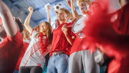 Fototapeta premium Sport Stadium Event: Crowd of Fans Cheer for Red Soccer Team to Win. People Celebrate Scoring a Goal, Championship Victory. Group of Friends with Painted Faces Have Fun. Low Angle Tribune SHot